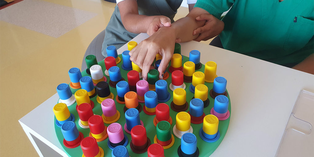 Mãos em exercício de coordenação com peças coloridas durante a terapia ocupacional.