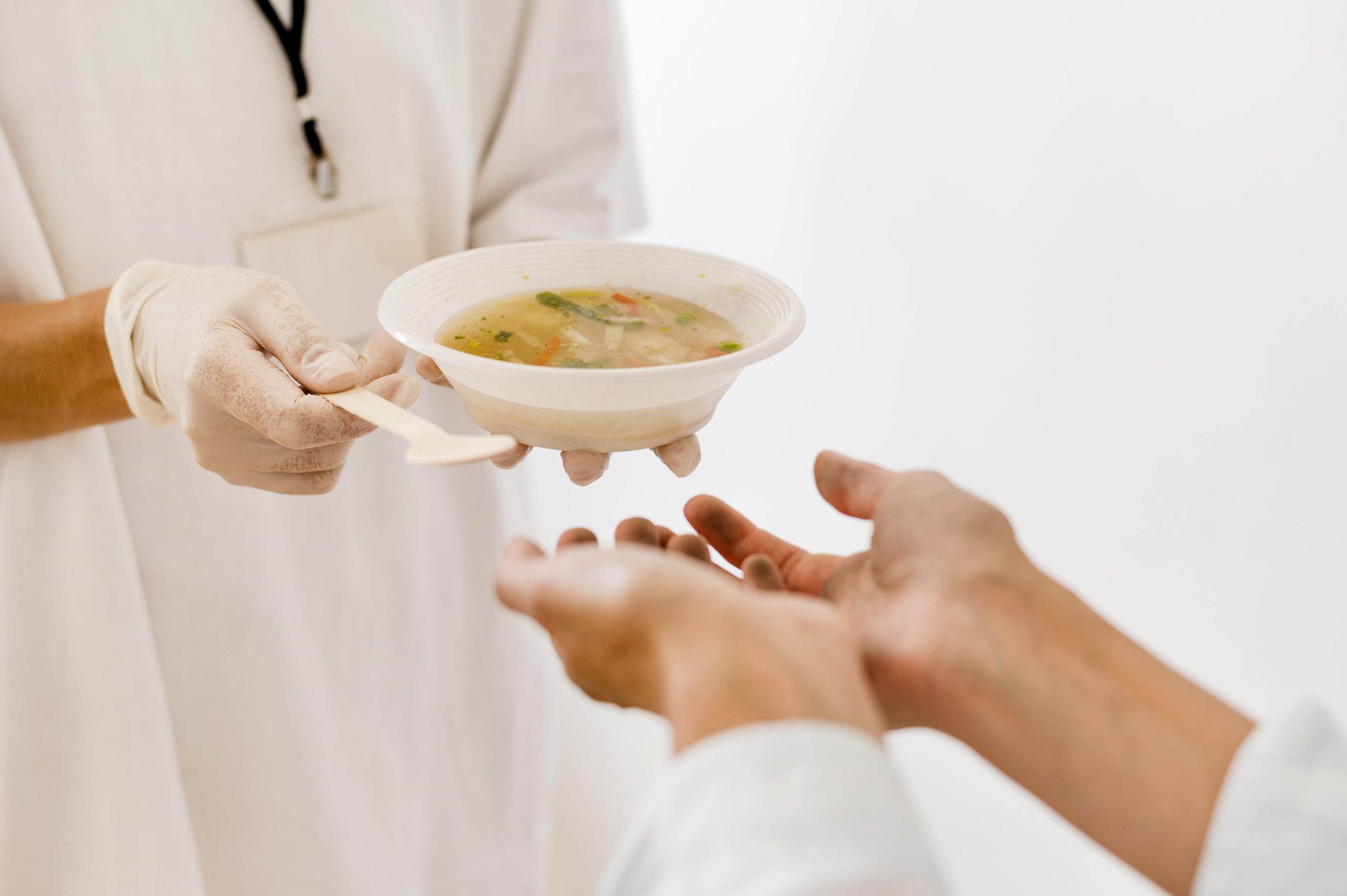 Profissional de saúde entrega porção de sopa a paciente durante oferta alimentar assistida.